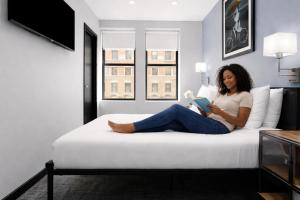 a woman sitting on a bed reading a book at OYO Times Square in New York
