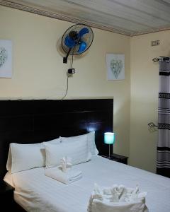 a bedroom with a bed with white sheets and a fan at Niyonest Guesthouse in Harare