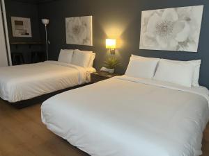 two beds in a hotel room with white pillows at Hôtel Normandie in Rimouski