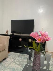 a living room with a tv and a vase with pink flowers at Suki Ruaka Homes in Ruaka +2 photos
