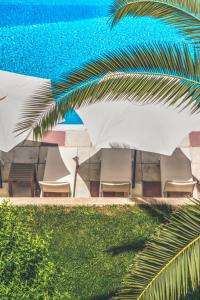 eine Gruppe von Stühlen und Sonnenschirmen neben einem Pool in der Unterkunft The Palm Garden in Ermones