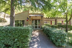 a building with a tree and bushes in front of it at Camping Verte Rive in Saint-Laurent-de-Cerdans