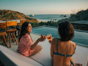 two women sitting on the edge of a pool with drinks at Casa Yute Boutique Hotel Playa Aragon in San Agustinillo