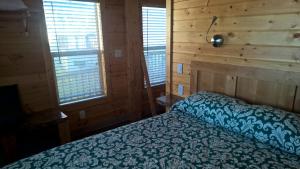 Cama en habitación con paredes y ventanas de madera en Lake Minden Camping Resort Cottage 1 en Nicolaus