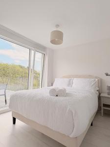 a white bedroom with a bed and a large window at 105 beach lodge millendreath in Looe