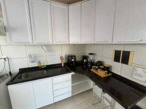 a kitchen with white cabinets and a black counter top at Apê mar e descanso com piscina no VOG JOÃO DE GOES ILHÉUS BA in Ilhéus
