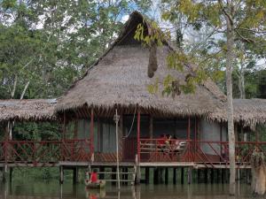 a house on the water with people sitting in it at CAMUNGO jungle Lodge in indigenous community ALL INCLUSIVE in Puerto Franco