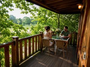a man and woman sitting at a table on the deck of a cabin at Les Chalets du Brusquand in Marquay