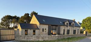 a stone house with a black roof and a stone wall at Chambre d'hôtes Lilas in Saint-Lyphard