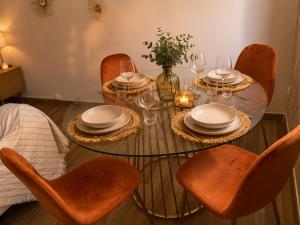 a glass table with chairs and plates and wine glasses at Evasion Terracotta - Jacuzzi privatif in Saint-Gaudens