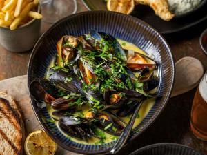 a bowl of mussels in a yellow sauce with a salad at Mercure Brighton Seafront Hotel in Brighton & Hove