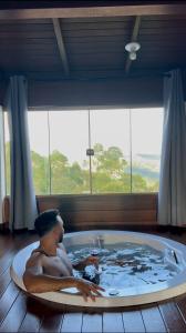 a man laying in a bath tub in front of a window at Chalés Mirante da Colina in Venda Nova do Imigrante +20 photos