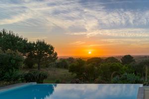 a swimming pool with a sunset in the background at Monte da Casa Telhada in Santiago do Cacém +47 photos