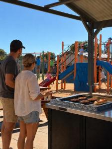 a man and a woman standing next to a grill at Sunset Beach Holiday Park in Geraldton