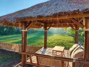 a straw hut with a table and a field at Nêst Guesthouse Tetebatu in Tetebatu