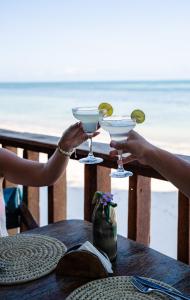 two people holding martini glasses at a table with the beach at ZAN Jambiani Beach House in Jambiani