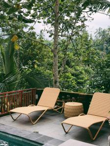 two chairs sitting on a deck next to a pool at Lira House by Yukaya Escape in Tegalalang