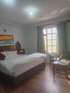 a bedroom with a bed and a chair and a window at Hotel Sidharth Tabo in Tabo