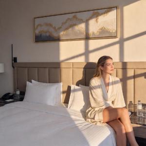 a woman sitting on a bed in a hotel room at Copthorne Hotel Sharjah in Sharjah
