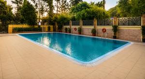 a swimming pool in a yard with a brick wall and trees at Pride Premier Pune in Pune
