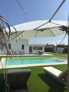 a swimming pool with a white umbrella and chairs at Villa Ikal in Modugno