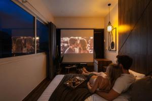 a man and woman sitting on a bed watching a tv at The Morris Central Hotel - O'TEL in Da Lat