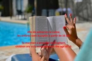a woman reading a book next to a pool at Les Jardins de Bormes, hôtel de charme et détente, espace bien-être avec sauna & jacuzzi in Bormes-les-Mimosas