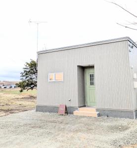 a building with a green door in a field at cottage hapo in Higashikagura