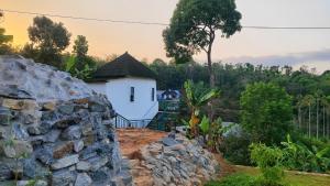 a white house with a stone wall in front of it at Rays of Bliss in Mananthavady