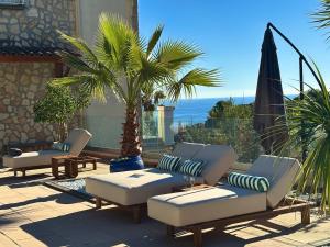 a patio with lounge chairs and a palm tree and the ocean at Sea View Villa Roc d'Azur - Pool - Jacuzzi in Vallauris