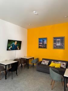 a waiting room with yellow walls and a couch and tables at Abay Hostel in Almaty