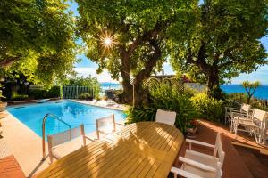 a wooden table and chairs next to a swimming pool at Hostdomus - Villa Gabriella with private pool in Alassio
