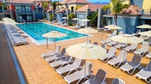 a group of chairs and umbrellas next to a swimming pool at Caybeach Meloneras in Meloneras