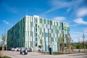 a glass building with cars parked in a parking lot at IBIS STYLES MUENCHEN AIRPORT in Munich