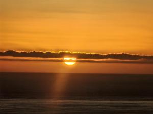 a sunset over the ocean with the sun hiding behind clouds at Panoramic Sea & Town View Oamaru 睁眼即见太平洋 I 躺观日月同辉 in Oamaru
