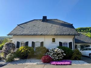 a white house with a black roof and some flowers at Moseloase am Weinberg mit Pool und Sauna in Bullay in Alf