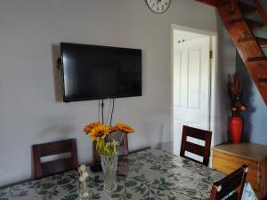 a dining room table with a vase of flowers and a television at Sea Wave Cottage in Pearly Beach