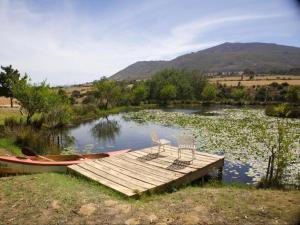a wooden dock with two chairs and a boat on a lake at Swaynekloof Farm in Botrivier