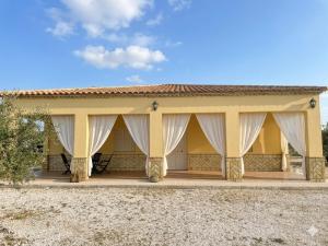 a yellow house with white curtains on the porch at Villa rural en Marchena in Marchena