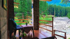 a porch with a table and a view of a forest at Celestia Riverside Retreat in Manāli