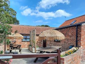 a patio with a wooden table and straw umbrellas at Harvest Cottage in Anderby
