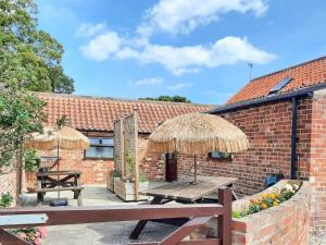 a patio with a wooden table and straw umbrellas at Plough Cottage in Anderby