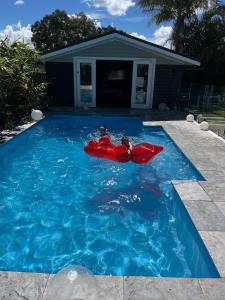 a couple of kids in a red raft in a swimming pool at Woy Woy Staycation - Heated Pool & Hot Tub & BBQ & Pizza Oven & Arcade Game & Pool Table in Woy Woy