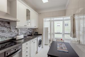 a white kitchen with a sink and a dishwasher at Almada Central by Homing in Almada