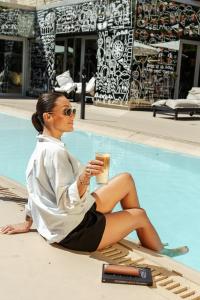 a woman sitting next to a swimming pool holding a drink at Casa Daupi Hotel Boutique in Mar del Plata