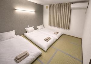 two beds in a room with white sheets at House Villa Koharu in Asahikawa