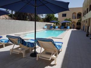 a pool with chairs and an umbrella and a table and chairs at Dandimayo Hotel Bar & Restaurant in Serekunda