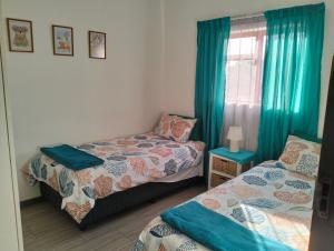 a bedroom with two beds and a window with blue curtains at Kosies Nest Gastehuis in Cape Town