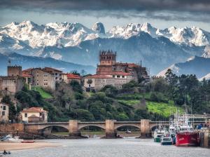 a town on a hill with a bridge and snowy mountains at Apartamento El Rey in Colombres