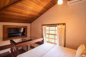 a bedroom with a bed and a tv and a window at Pousada Villaggio Assis in Ilhabela